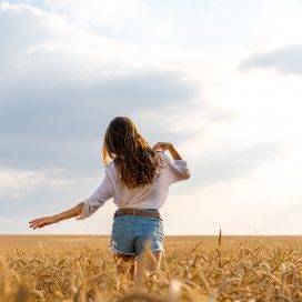 a beautiful young woman stands in a field of wheat with developing hair in the wind against the sky